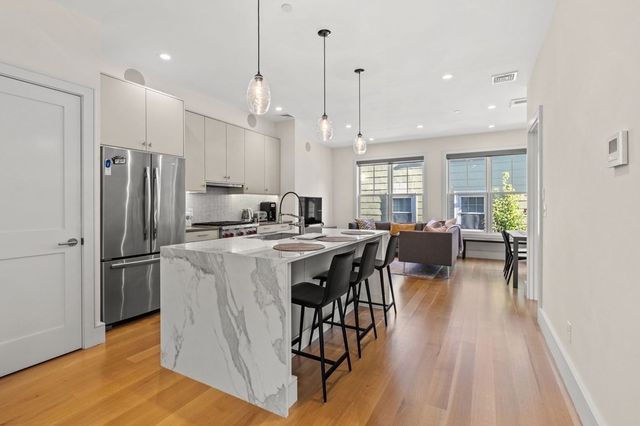 a kitchen with stainless steel appliances granite countertop a refrigerator a sink a stove a dining table and chairs with wooden floor