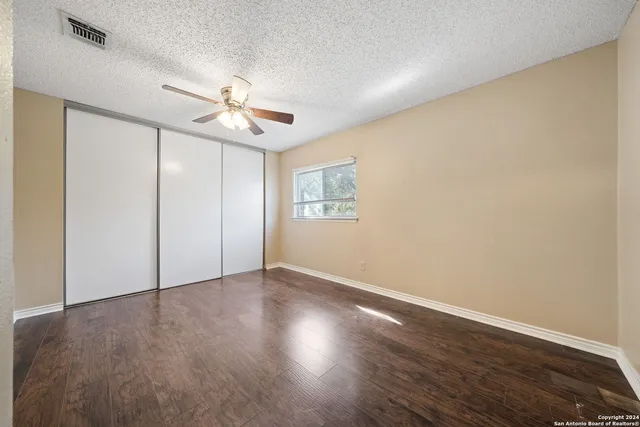 an empty room with wooden floor ceiling fan and windows