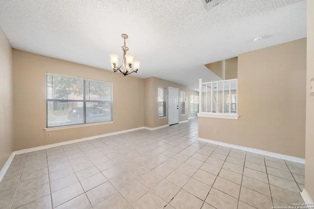 a view of an empty room with window and chandelier fan