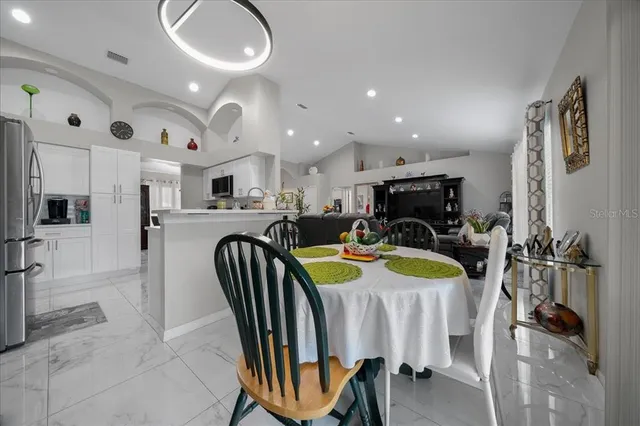 a kitchen with stainless steel appliances kitchen island granite countertop a dining table chairs and a refrigerator