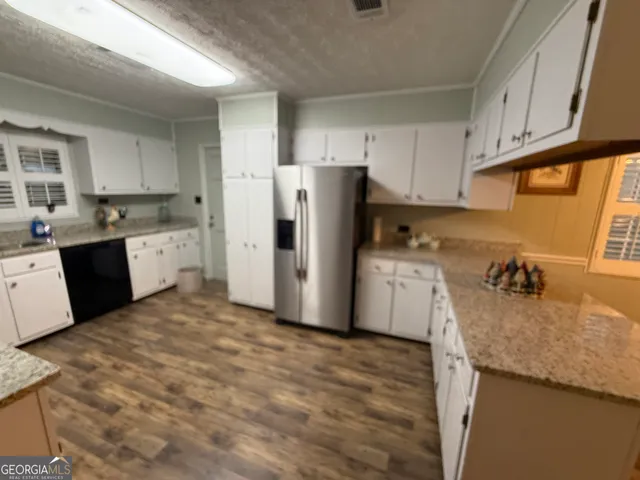 a kitchen with granite countertop a refrigerator a sink dishwasher and white cabinets with wooden floor