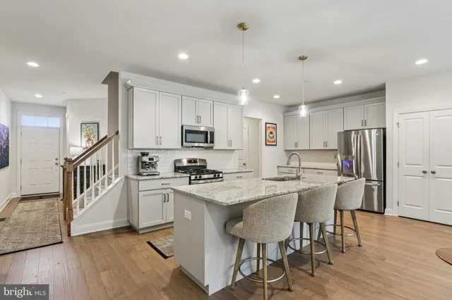 a kitchen with stainless steel appliances kitchen island granite countertop a stove a sink a refrigerator white cabinets and wooden floor