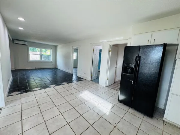 a view of a refrigerator in kitchen and an empty room and wooden floor