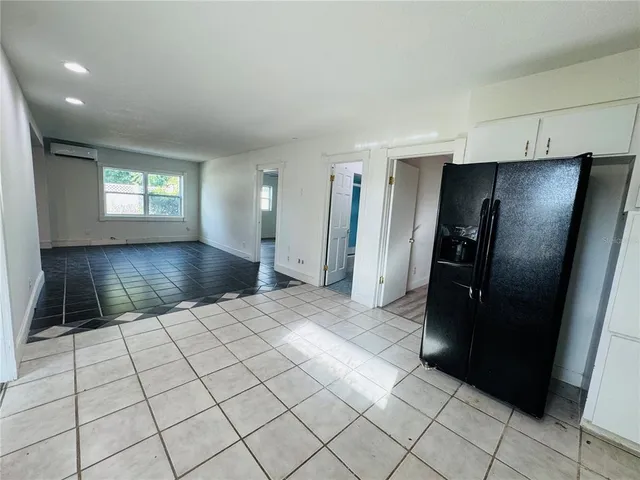 a view of a refrigerator in kitchen and an empty room and wooden floor