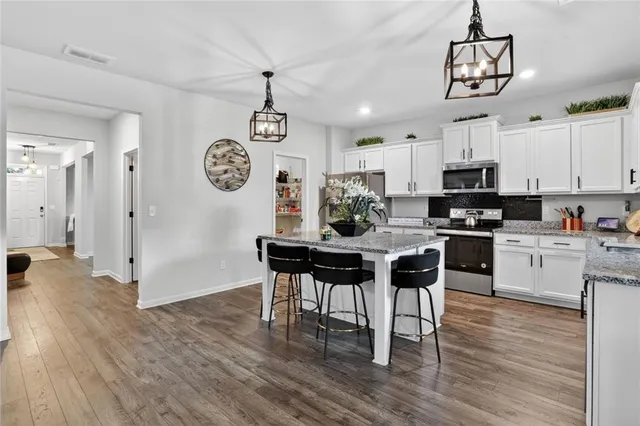 a kitchen with stainless steel appliances granite countertop a stove a refrigerator a sink a dining table and chairs with wooden floor