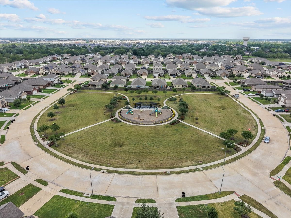 2320 Rosemary Street Rosenberg, TX 77469 - Photo 25 of 40 This aerial photo showcases a suburban neighborhood with a circular park at its center, featuring a playground surrounded by well-kept lawns and sidewalks. The area is lined with neatly arranged houses, offering a family-friendly and community-oriented atmosphere.