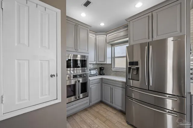 a kitchen with stainless steel appliances granite countertop a refrigerator oven a sink and white cabinets with wooden floor