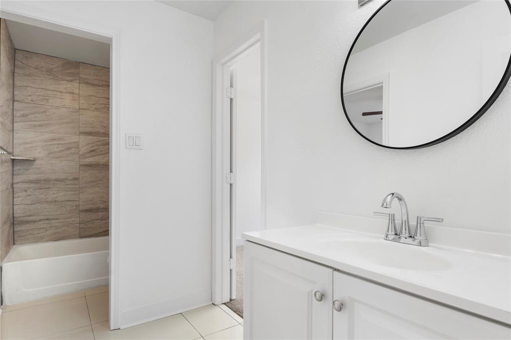 559 Raintree Circle Coppell, TX 75019 - Photo 28 of 40 Bathroom featuring a white vanity with integrated sink, chrome faucet, and a round black-framed mirror