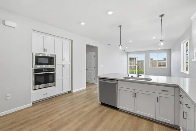 a kitchen with stainless steel appliances granite countertop a refrigerator a sink dishwasher and white cabinets with wooden floor