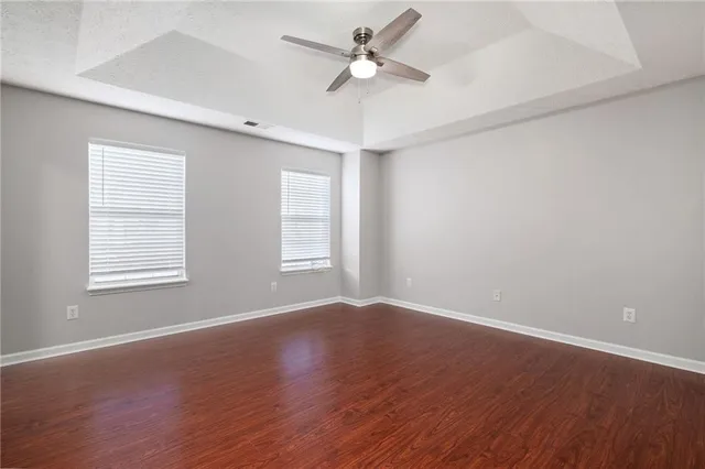 an empty room with wooden floor ceiling fan and windows