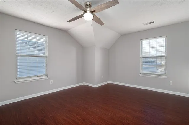 an empty room with wooden floor ceiling fan and windows