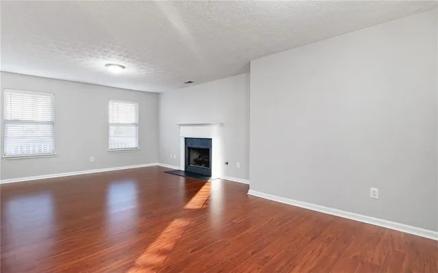 an empty room with wooden floor fireplace and windows