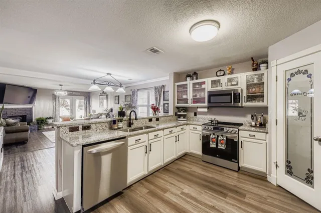 a kitchen with stainless steel appliances granite countertop a stove top oven a sink dishwasher and a refrigerator with wooden floor