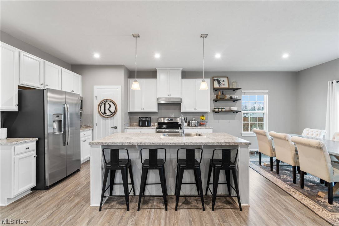 524 Oliver Way Rittman, OH 44270 - Photo 11 of 33 Kitchen with light wood-style flooring, a kitchen island with sink, stainless steel fridge, pendant lighting, and white cabinetry