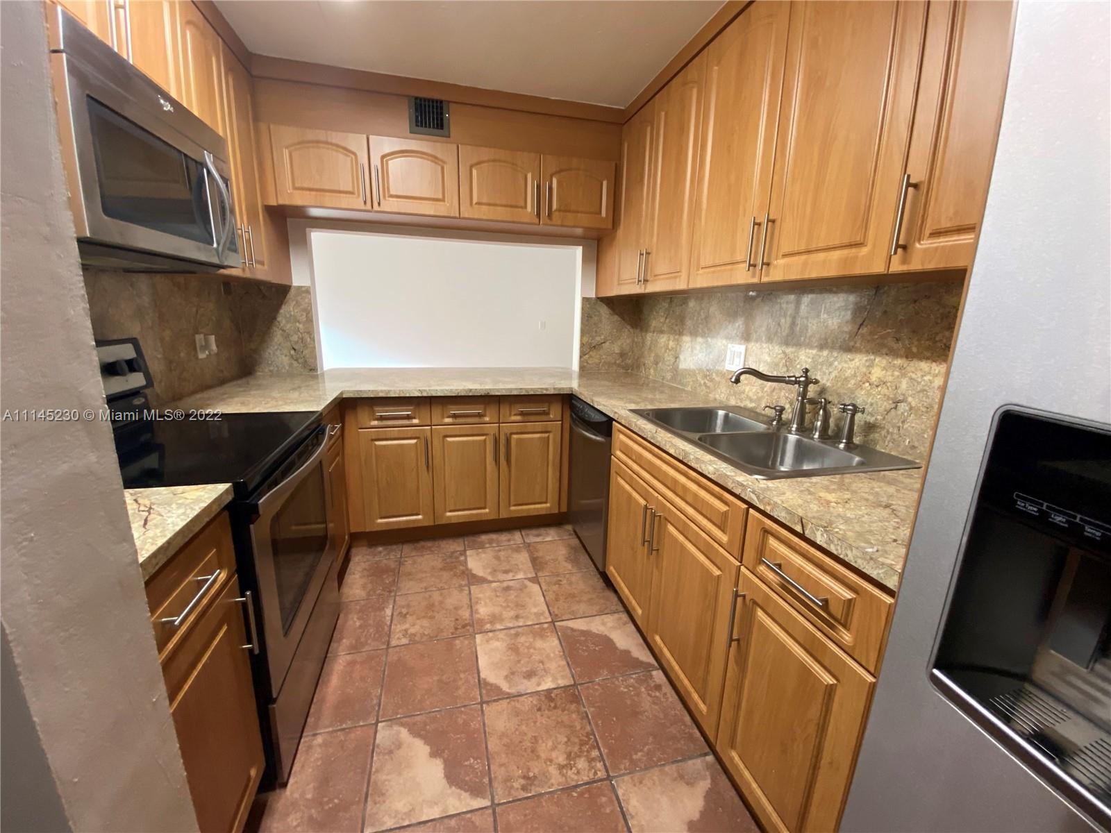a kitchen with granite countertop a sink a stove top oven and cabinetry