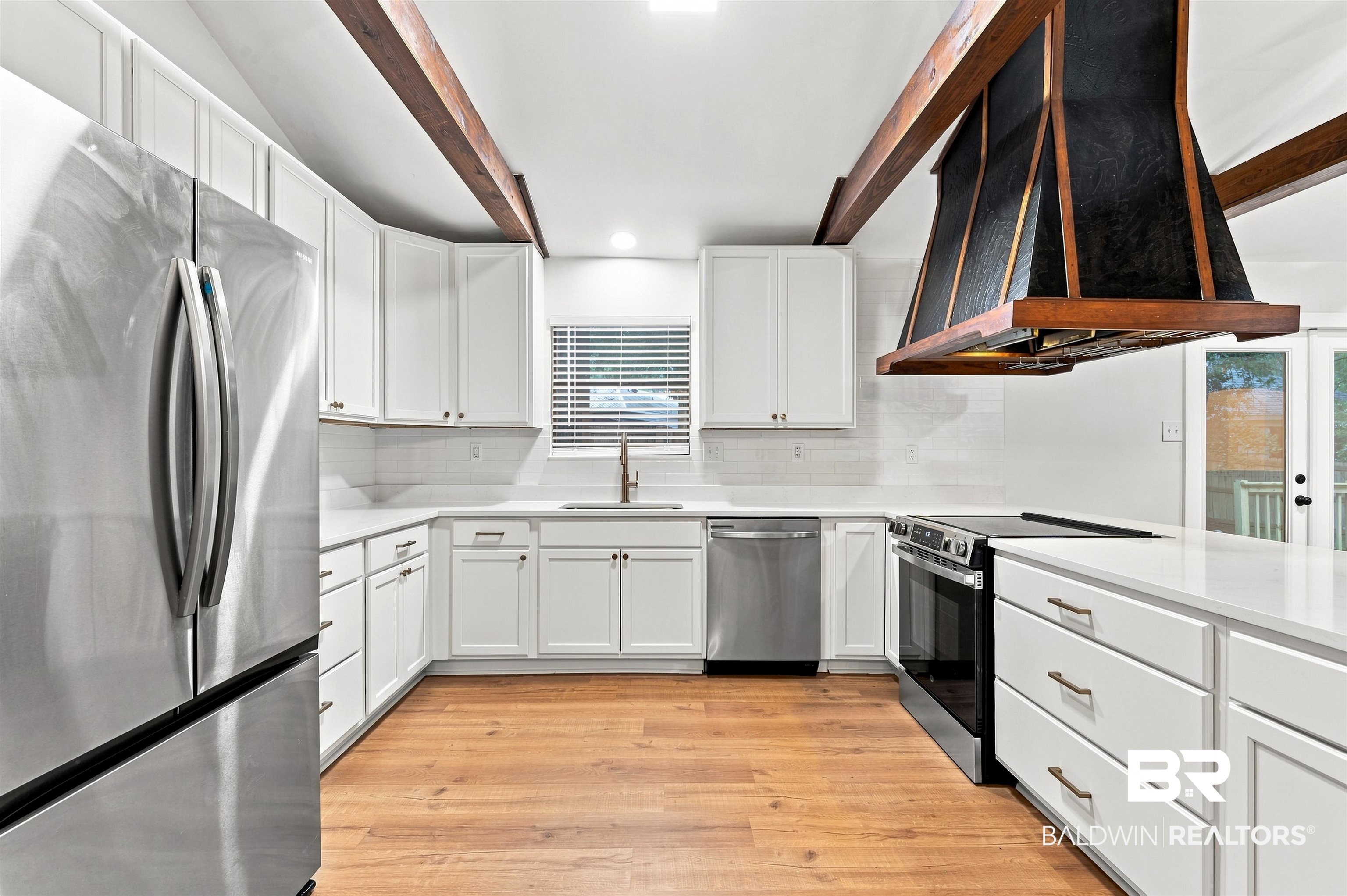 599 Ridgewood Drive Daphne, AL 36526 - Photo 10 of 41 Modern kitchen with white cabinetry, stainless steel appliances, wood-finish flooring, exposed ceiling beams, and a custom range hood