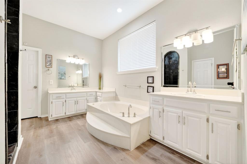 4509 Scenic Drive Rowlett, TX 75088 - Photo 24 of 40 Spacious bathroom featuring a built-in soaking tub, dual vanity areas with white cabinetry and integrated sinks, wood-finish flooring, and a shower enclosure with black tile