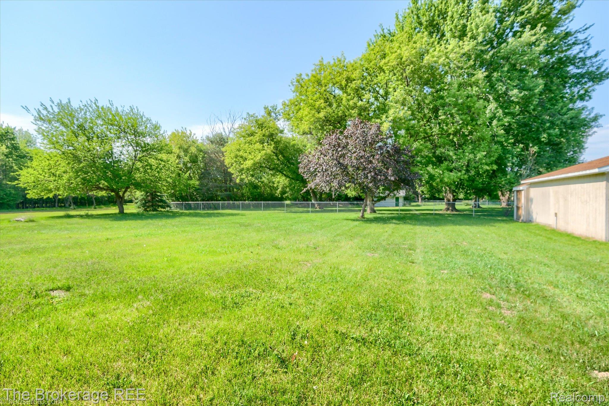 5495 East Coldwater Road Flint, MI 48506 - Photo 8 of 44 Expansive green lawn featuring mature trees, a chain-link fence, and a neutral-toned outbuilding