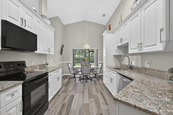 a kitchen with granite countertop a sink dishwasher stove and white cabinets with wooden floor