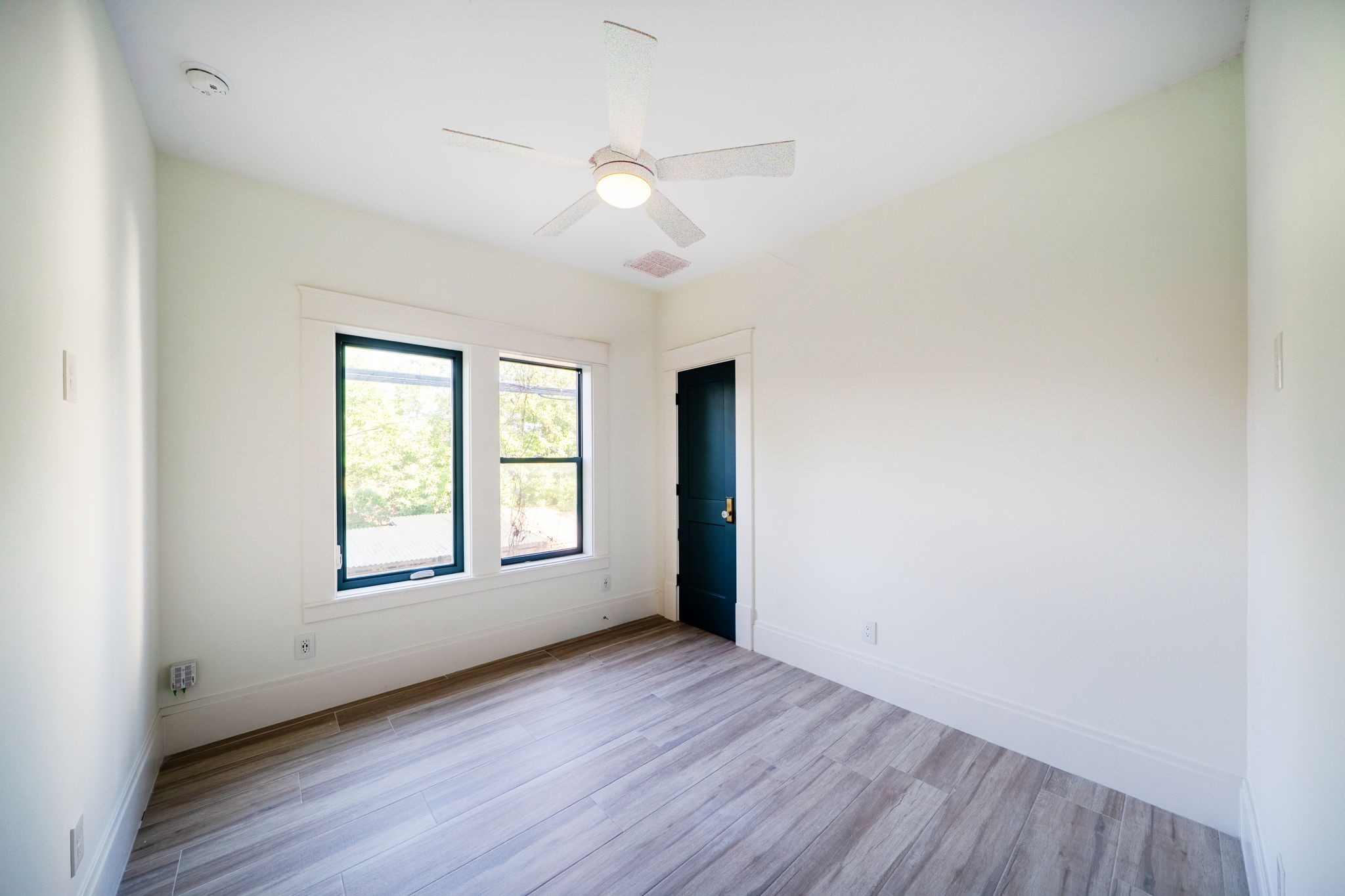 1109 Rutland Street Houston, TX 77008 - Photo 29 of 34 Bright, minimalist room with light wood flooring and a ceiling fan. Features two large windows for natural light and a contrasting d door, creating a modern contrast.