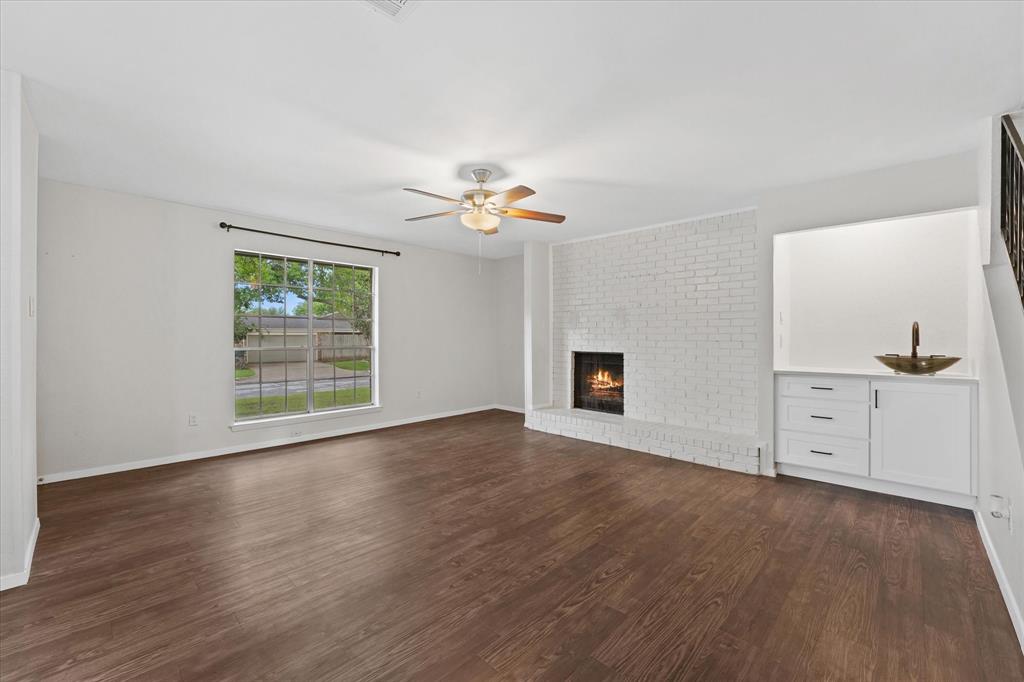 4007 Ridgebrook Drive Arlington, TX 76015 - Photo 4 of 18 Spacious living area featuring dark wood-finish flooring, a white painted brick fireplace, and a built-in cabinetry unit with a white countertop