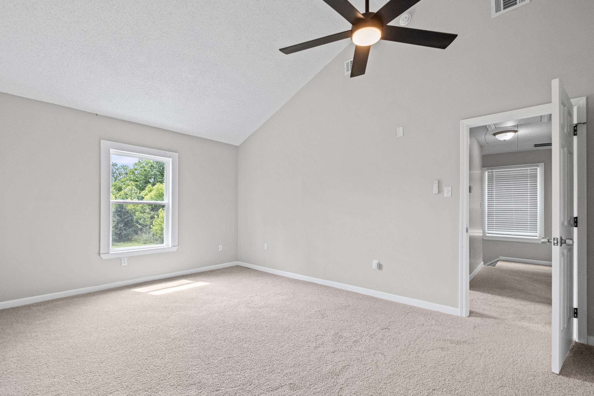 5843 Stewart Road Lakeland, TN 38002 - Photo 17 of 26 Spacious room featuring vaulted ceilings, light-toned carpeting, a large window with white trim, and a ceiling fan with integrated lighting