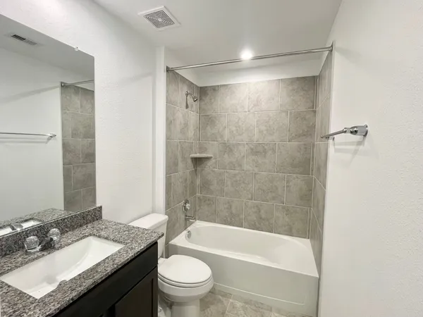 a bathroom with a granite countertop sink a toilet a mirror and bathtub