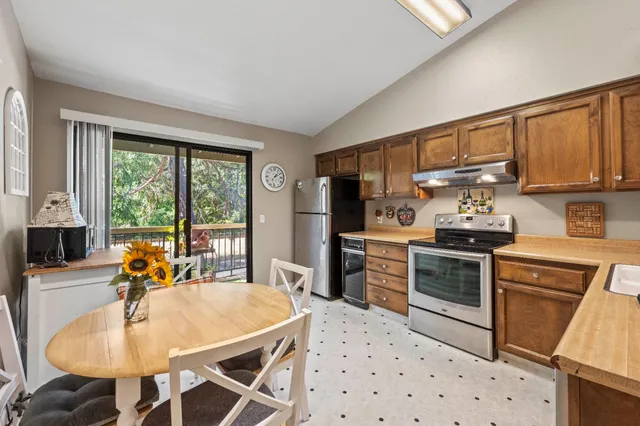 a kitchen with stainless steel appliances granite countertop a stove a refrigerator a sink dishwasher a dining table and chairs with wooden floor
