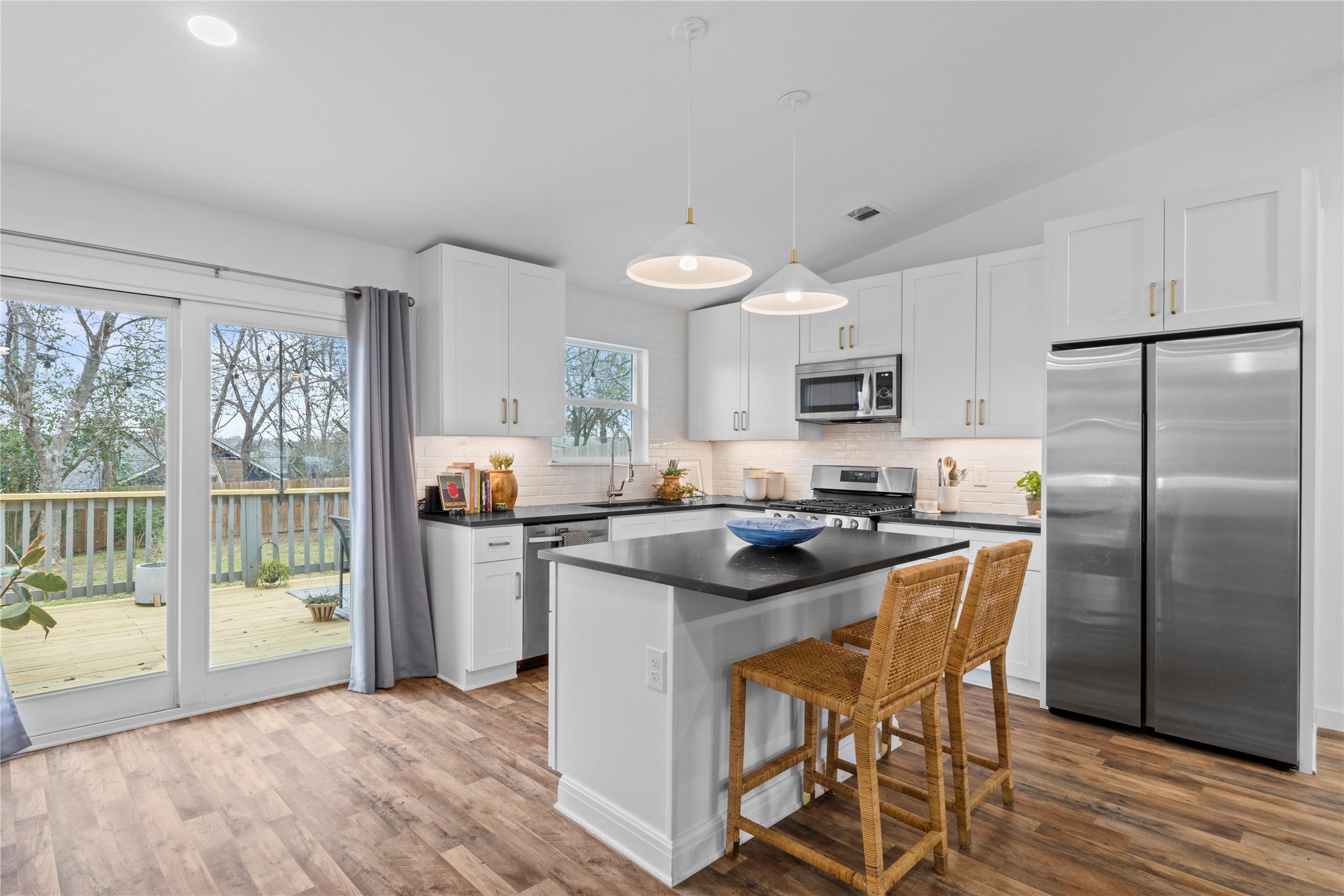 6809 Roanoke Drive Austin, TX 78723 - Photo 6 of 25 Kitchen with stainless steel appliances, hanging light fixtures, a kitchen bar, white cabinets, and lofted ceiling