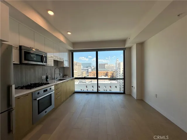 a kitchen with stainless steel appliances a stove top oven a sink a refrigerator with wooden floor and cabinets