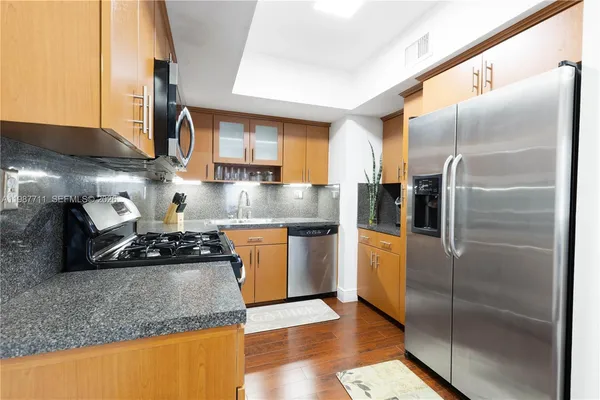 a kitchen with stainless steel appliances granite countertop a refrigerator a stove and a sink with wooden floor