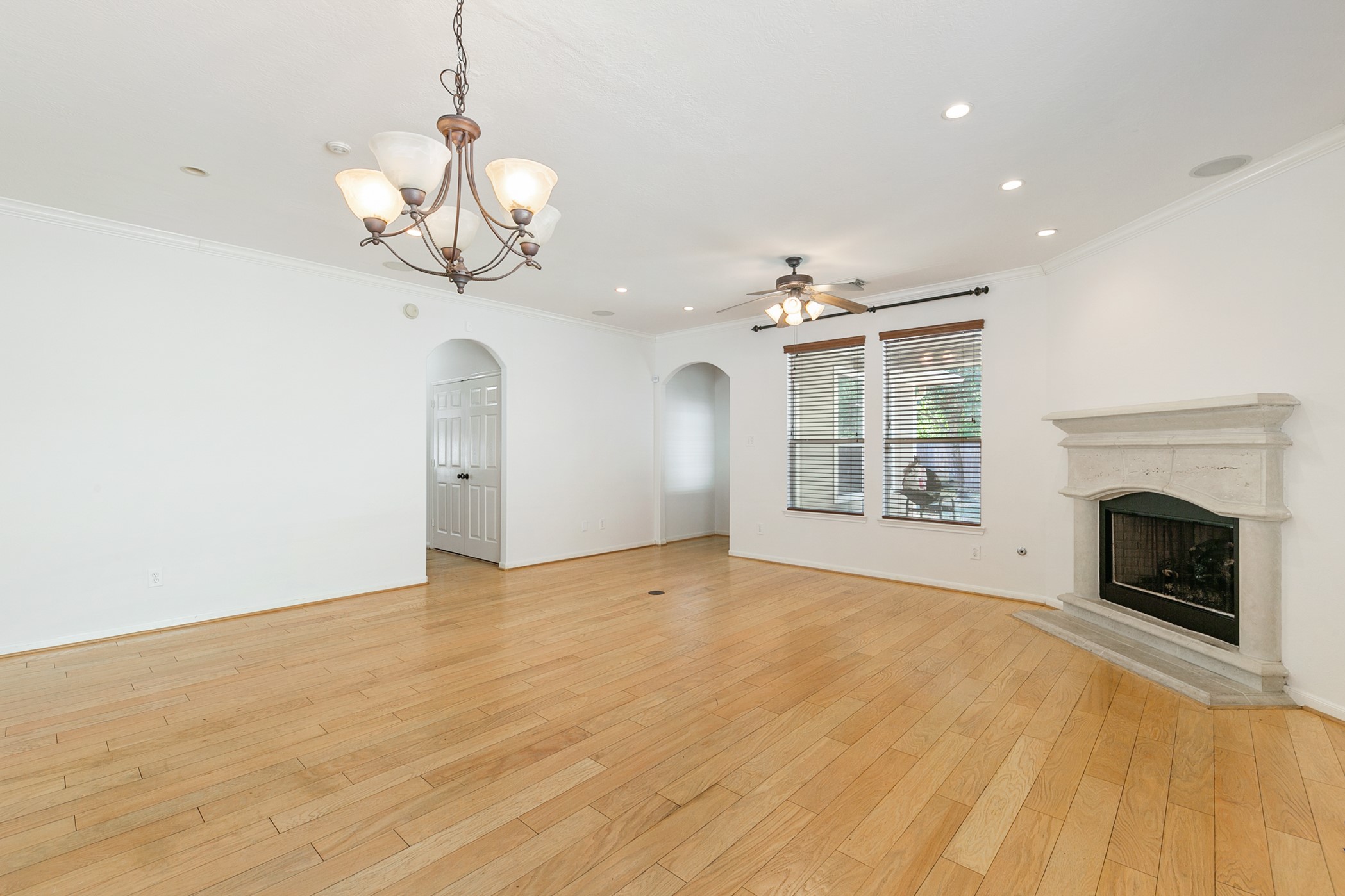 24527 Spring Harbor Drive Spring, TX 77373 - Photo 10 of 22 This spacious living room features hardwood floors, a cozy fireplace, and ample natural light from large windows. It includes a ceiling fan, recessed lighting, and a stylish chandelier, with arched doorways adding elegant charm.