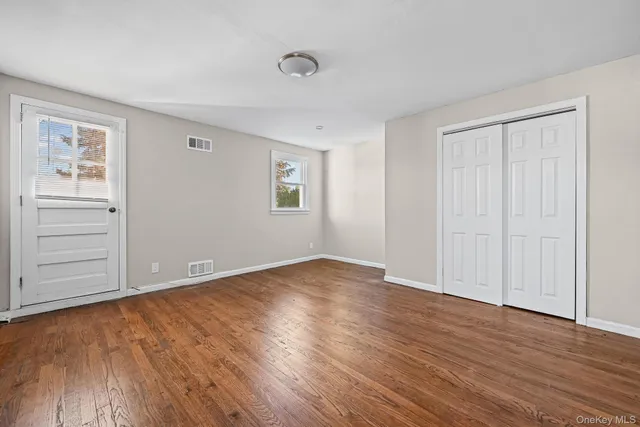 an empty room with wooden floor closet and windows