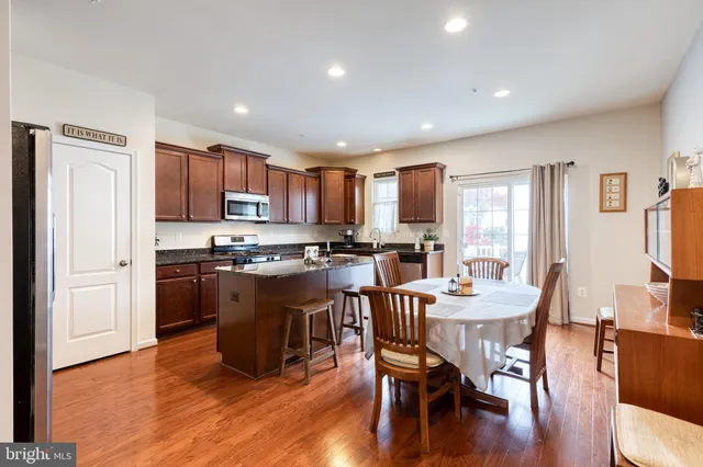 a kitchen with stainless steel appliances granite countertop a refrigerator a stove top oven a sink dishwasher and a dining table with wooden floor