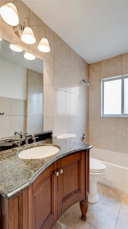 a bathroom with a granite countertop sink a toilet a mirror and bathtub