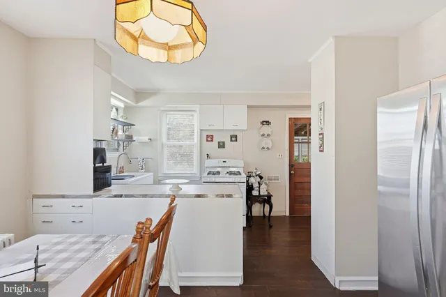 a living room with stainless steel appliances kitchen island granite countertop a refrigerator a stove and white cabinets with wooden floor