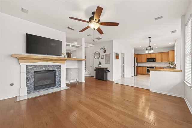 a view of a livingroom with a fireplace a ceiling fan and a kitchen view