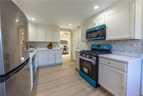 a kitchen with stainless steel appliances a stove top oven a sink a refrigerator white cabinets and wooden floor