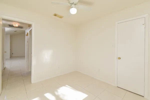an empty room with a chandelier fan and kitchen view