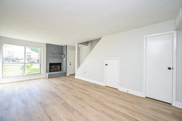 an empty room with wooden floor fireplace and windows