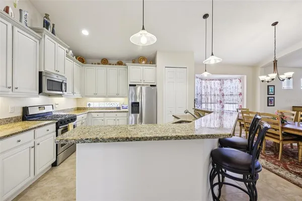 a kitchen with stainless steel appliances granite countertop a sink a stove a refrigerator a dining table and chairs with wooden floor