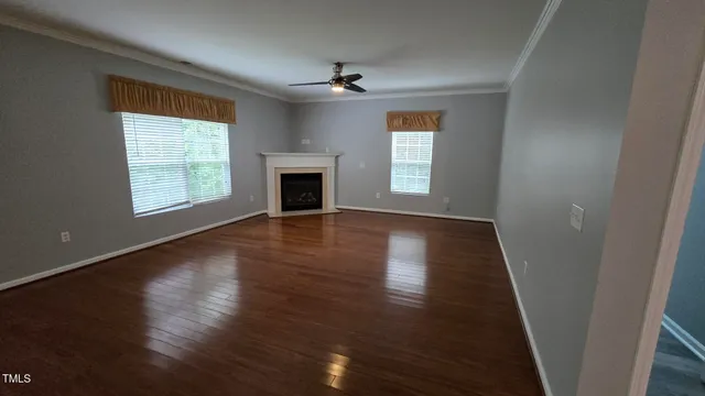 an empty room with wooden floor fireplace and windows