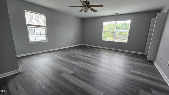 an empty room with wooden floor chandelier fan and windows