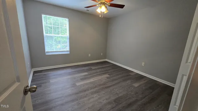 an empty room with wooden floor chandelier fan and windows
