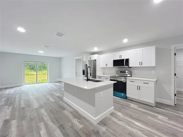 a large white kitchen with a stove a sink dishwasher and a refrigerator with wooden floor