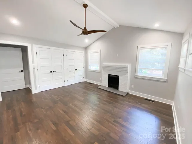 an empty room with wooden floor fireplace and windows