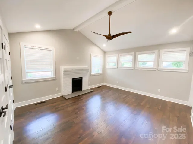 an empty room with wooden floor fireplace and windows