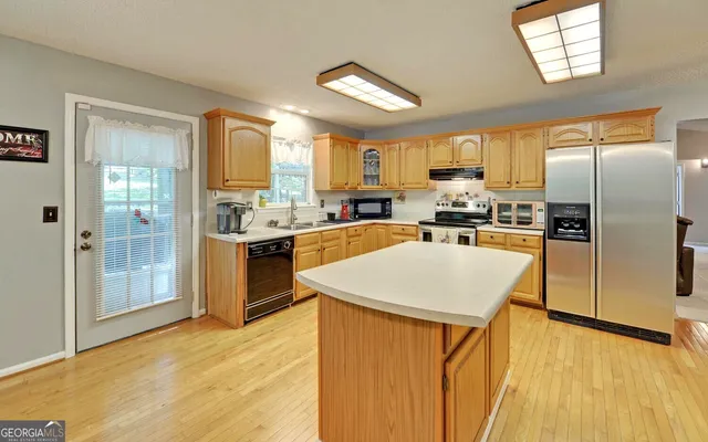 a kitchen with stainless steel appliances granite countertop a refrigerator a sink a stove and white cabinets with wooden floor