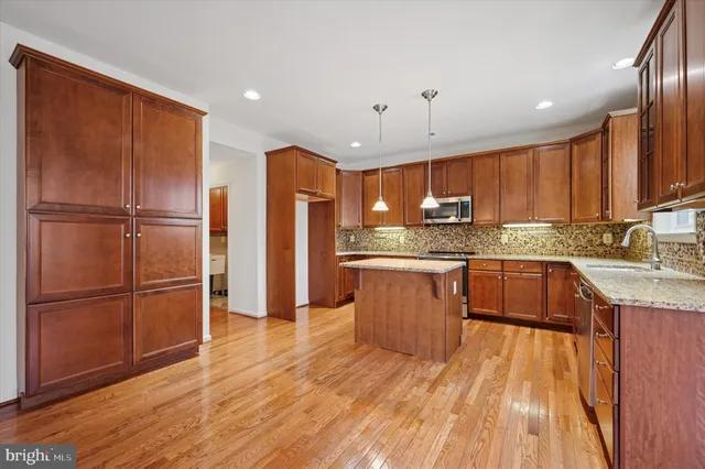 a kitchen with kitchen island granite countertop wooden floors stainless steel appliances a sink and a refrigerator
