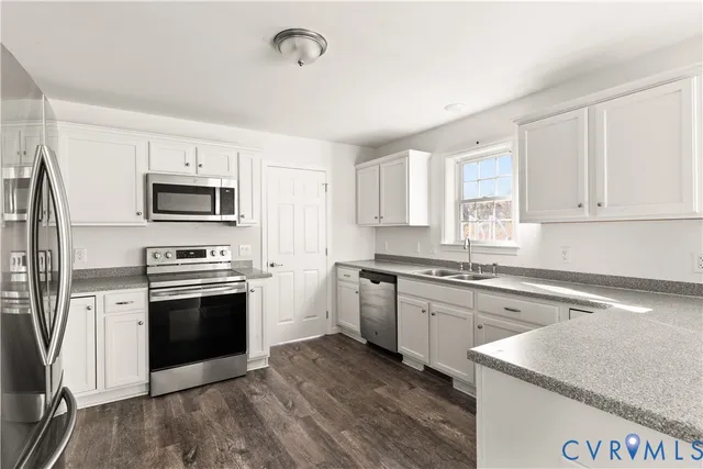 a kitchen with stainless steel appliances granite countertop a stove top oven a sink dishwasher a refrigerator and a microwave oven with white cabinets